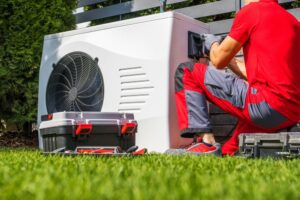 A man sitting on the grass next to an air conditioner.