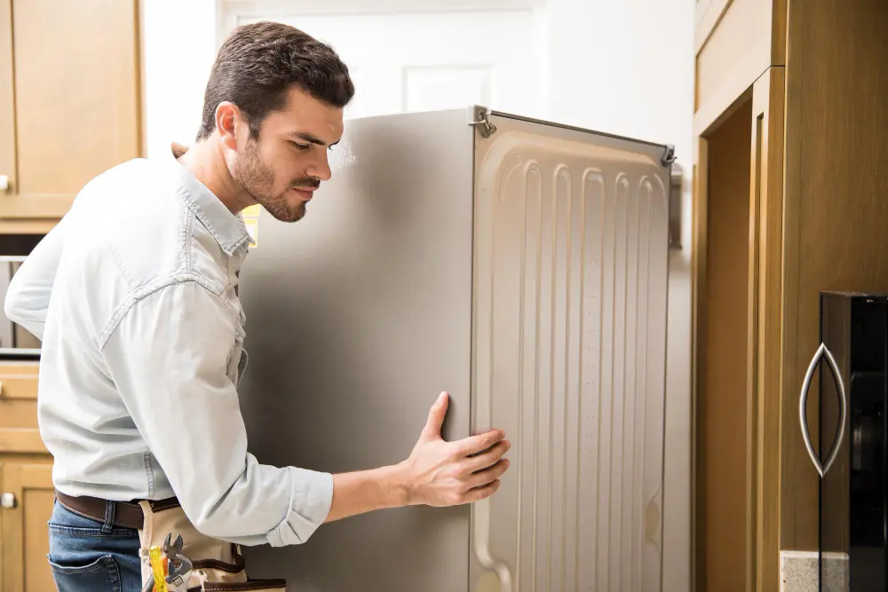 A man is holding the door of an old refrigerator.