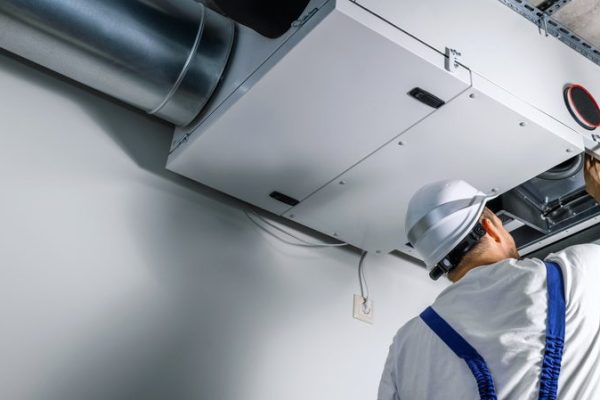 A man in white hard hat standing next to an air conditioner.